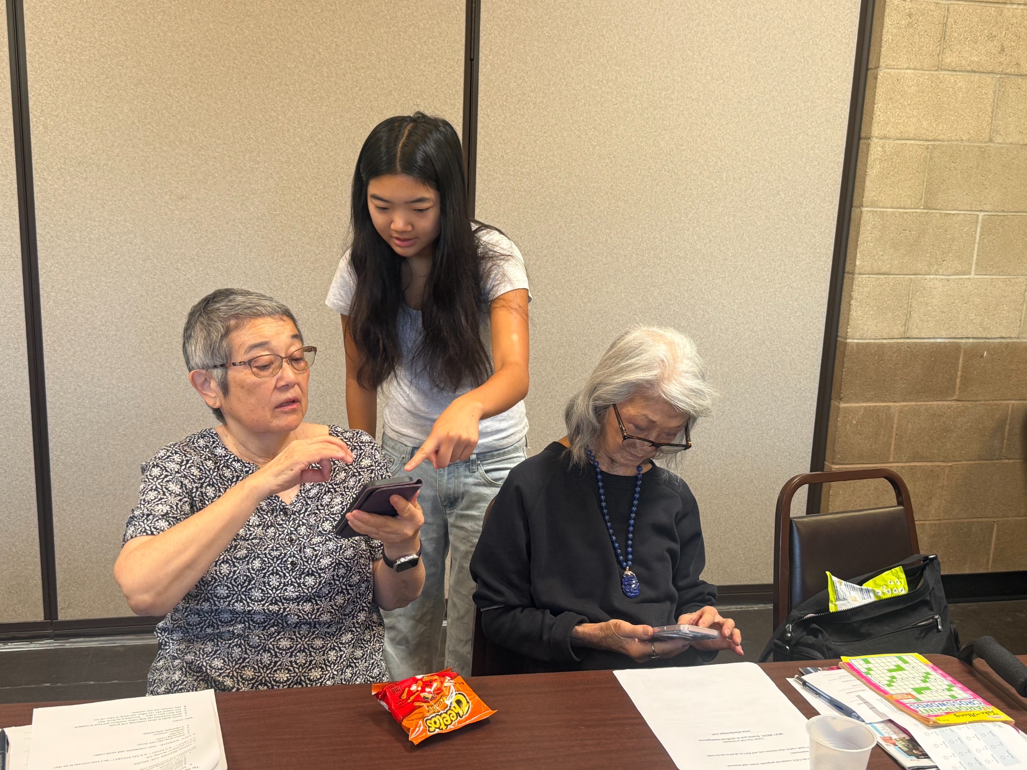 A volunteer helping two seniors use their phones